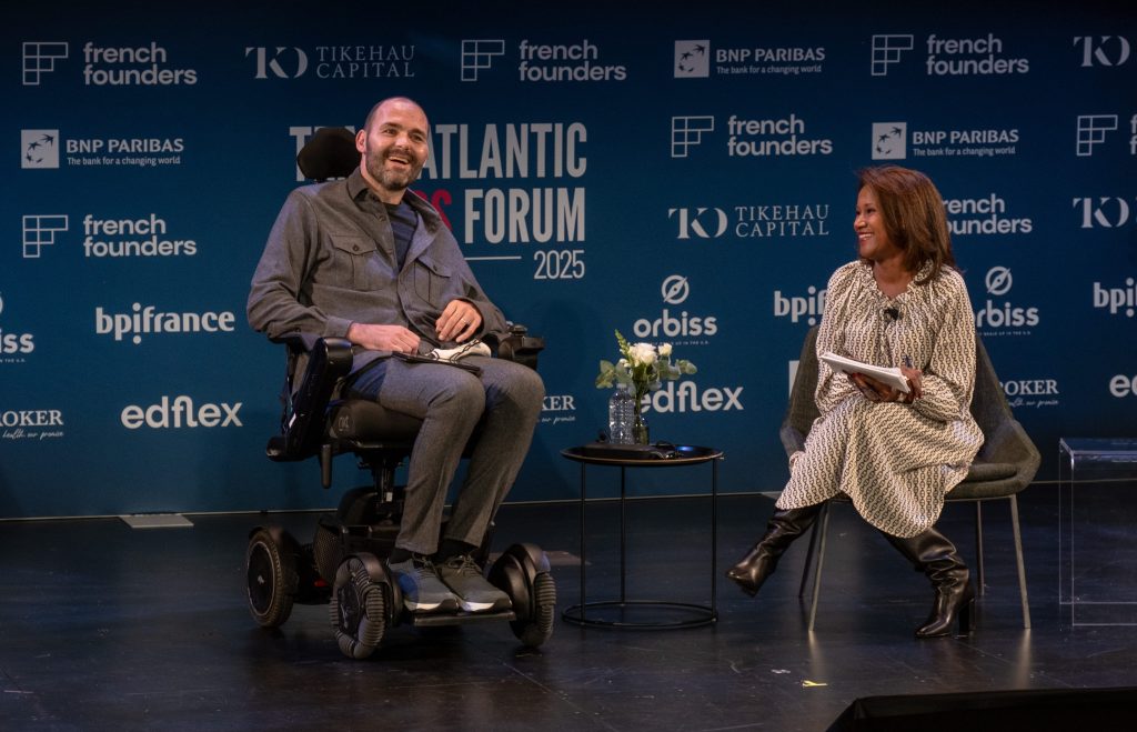 Olivier Goy, an ALS patient, speaking on stage during the Transatlantic Leaders Forum 2025, while Magalie Laguerre-Wilkinson listens.