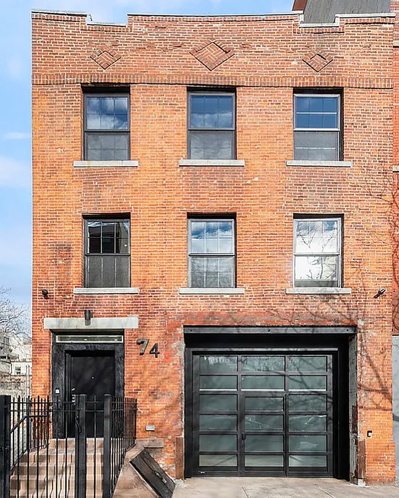 A brick building featuring large black-framed windows and a glass garage door, with the number '74' prominently displayed above the entrance.