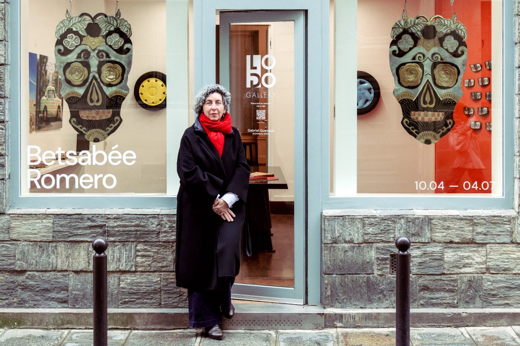 A woman stands outside the Lobo Gallery, wearing a black coat and red scarf, with a decorative skull artwork visible in the window.