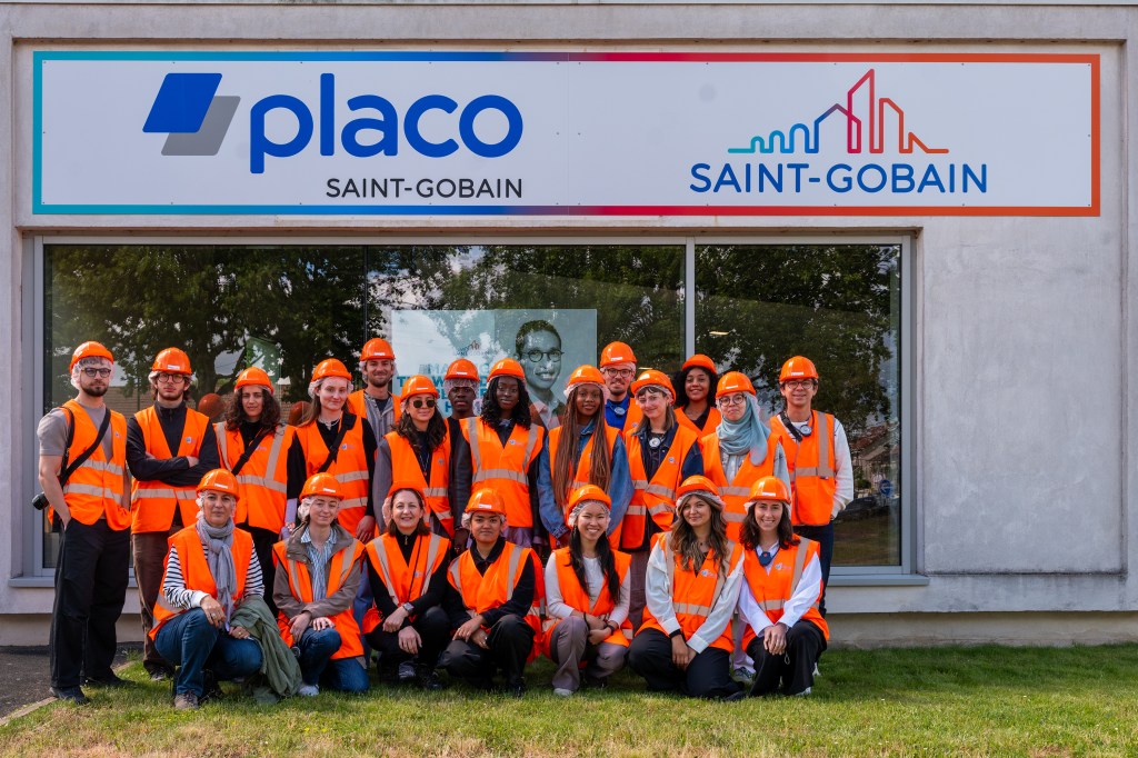 A diverse group of people wearing safety vests and hard hats posing in front of a Placo Saint-Gobain sign.