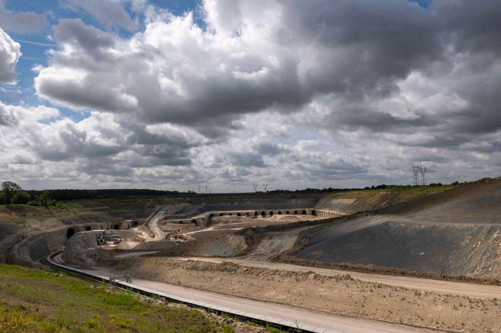 A large open-pit mining site with multiple excavations, surrounded by rolling hills and cloudy skies.